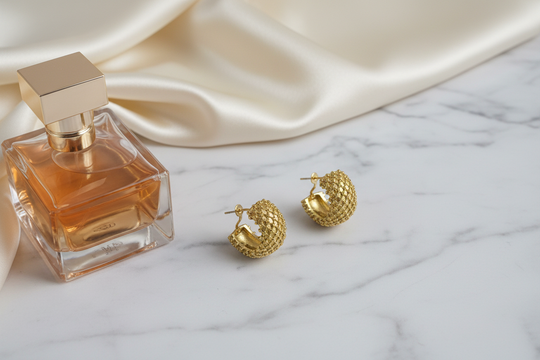 Gouden creool oorbellen bolletjes op wit marmer met satijn en parfum