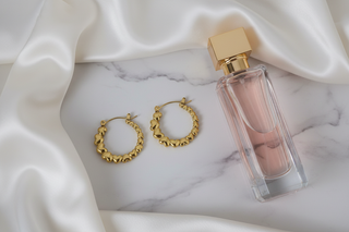 Gouden creool oorbellen hartjes op wit marmer met satijn en parfum