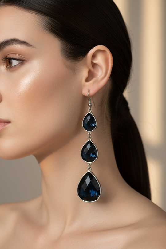 Model draagt lange druppel oorbellen met donkerblauwe kristallen